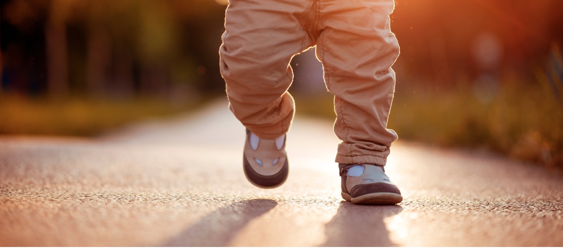 imagen de los pies de un bebé corriendo sobre el pavimento al atardecer